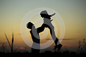Silhouette of father throwing up his happy daughter in the air at sunset.