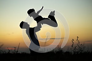 Silhouette of father throwing up his happy daughter in the air at sunset.