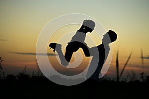 Silhouette of father throwing up his happy daughter in the air at sunset