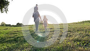 Silhouette of father with two children walking into sunset at meadow