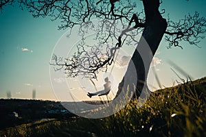 Silhouette of a female enjoying the sunset on a tree swing on a mountainous area