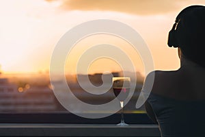 Silhouette of female hand with glass of red wine on the sunset town background