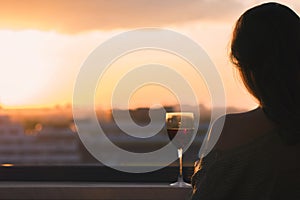 Silhouette of female hand with glass of red wine on the sunset town background