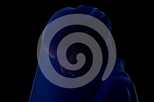 Silhouette of female head under blue veil on black background