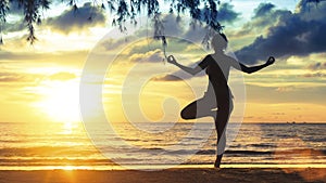 Silhouette female practicing yoga on the beach at magnificent sunset.