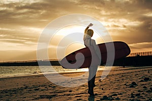 silhouette of female surfer posing with surfboard at sunset