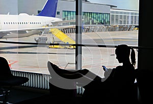 SILHOUETTE Female tourist waiting for her flight and playing games on smartphone