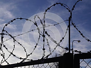 Silhouette of a fence with barbed wire against a blue sky. Prison security.