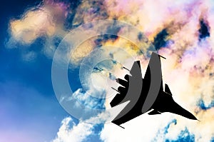Silhouette of a fighter plane on a background of iridescent sky clouds and sun