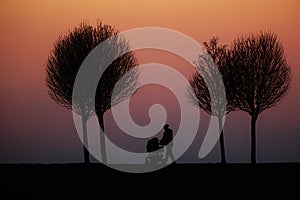 Silhouette of a figure with a stroller walking along a road against a red-purple sky just after sunset