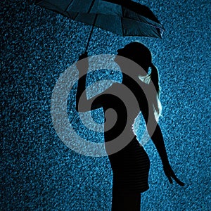 Silhouette of the figure of a young girl with an umbrella in the rain, a young woman with hand-picked hair is happy to drops of