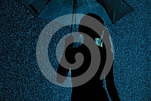 Silhouette of the figure of a young girl with an umbrella in the rain, a young woman with hand-picked hair is happy to drops of