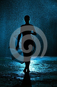 Silhouette of the figure of a young girl with an umbrella in the rain, a young woman happy to drops of water