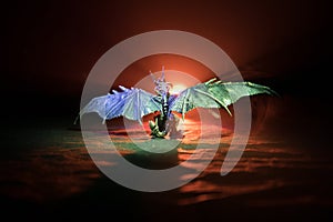 Silhouette of fire breathing dragon with big wings on a dark orange background. Horror image