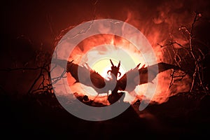 Silhouette of fire breathing dragon with big wings on a dark orange background. Horror image