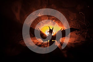 Silhouette of fire breathing dragon with big wings on a dark orange background. Horror image