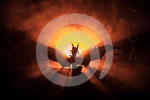 Silhouette of fire breathing dragon with big wings on a dark orange background. Horror image
