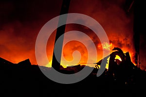 Silhouette of Firemen fighting a raging fire with huge flames