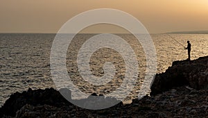 Silhouette of a fisher fisheman fishing in the ocean at sunset