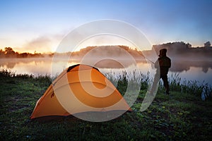 Silhouette fisherman on background of orange tent on shore