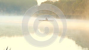 Silhouette of a fisherman in a boat. Fog over the morning river in the forest. Cross the lake by boat.