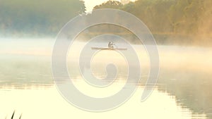 Silhouette of a fisherman in a boat. Fog over the morning river in the forest. Cross the lake by boat.