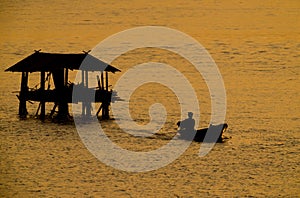 Silhouette of fisherman boat go out from fisherman`s cottage in river