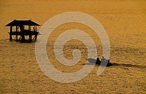 Silhouette of fisherman boat heading towards fisherman`s cottage in river