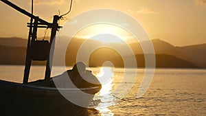 Silhouette of a fisherman in a calm sea at dawn. Beautiful sunset at the sea with a fishing boat silhouettes on the