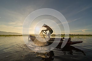 Silhouette Fisherman casting or throwing a net for catching freshwater fish in nature lake or river with reflection in morning