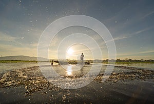 Silhouette Fisherman casting or throwing a net for catching freshwater fish in nature lake or river with reflection in morning