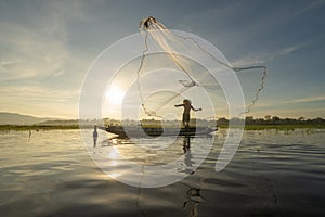 Silhouette Fisherman casting or throwing a net for catching freshwater fish in nature lake or river with reflection in morning