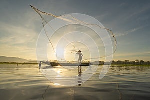 Silhouette Fisherman casting or throwing a net for catching freshwater fish in nature lake or river with reflection in morning