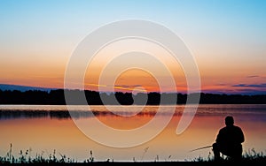 Silhouette of a fisherman with a fishing rod in the morning on a fishing trip. Peaceful sunrise on lake