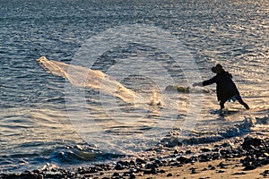 silhouette of fisherman pulling his trammel net on the beach shore, during sunset
