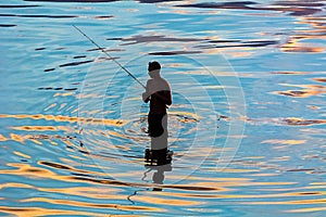 Silhouette of a fisherman in reflection in water ripples