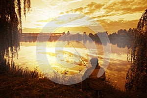 Silhouette of fisherman sitting on shore of lake at sunset