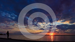 Silhouette of a fisherman standing on a sunset background landscape