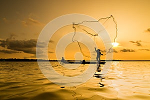 Silhouette of a fisherman throwing his net with sunset.