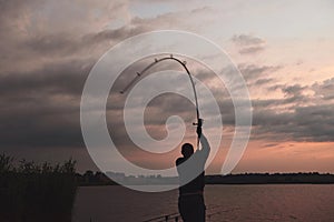 Silhouette of fisherman throws a fishing pole into the lake at sunset
