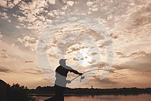 Silhouette of fisherman throws a fishing pole into the lake at sunset