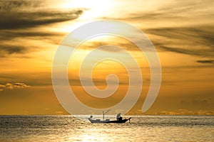 Silhouette of fishermen in the boat on sea with yellow and orange sun in the background