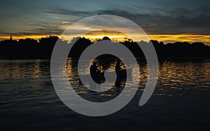 Silhouette of fishermen pedalling their boat at sunset cloudy golden sky background