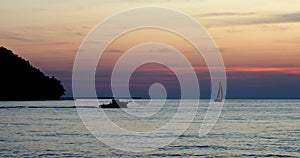 Silhouette of a fishing boat motoring past a sailboat at twilight