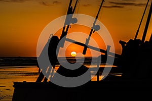 Silhouette of a fishing boat with fishing rods and reels with a golden sunset.