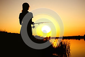 Silhouette of a fishing woman on the river bank on the nature at dawn