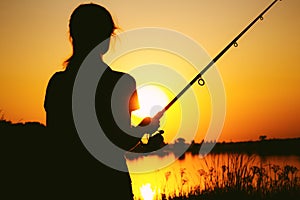 Silhouette of a fishing woman on the river bank at sunset