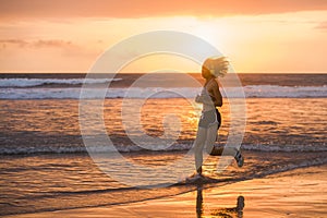 Silhouette of fit and athletic Asian Chinese sporty woman running on beautiful beach doing jogging workout on sunset in fitness he