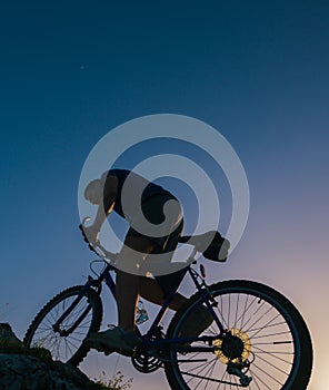 Silhouette of a fit male mountain biker riding his bike uphill on rocky harsh terrain on a sunset