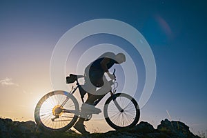 Silhouette of a fit male mountain biker riding his bike uphill on rocky harsh terrain on a sunset